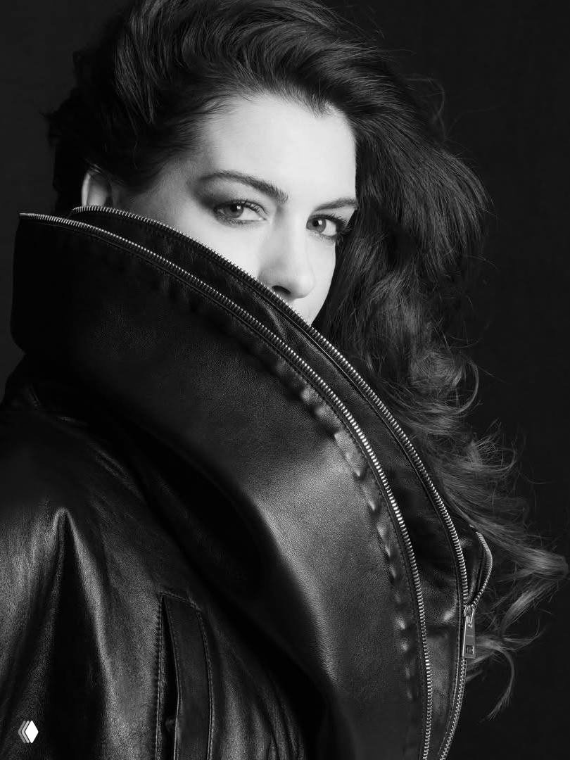 Чёрно-белый студийный портрет женщины в объёмной кожаной куртке с высоким воротником, частично скрывающим лицо, драматическое освещение.