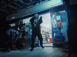 Ночной кадр у входа в магазин: несколько человек в масках и спортивной одежде в движении, сцена снята с низкой точки обзора.