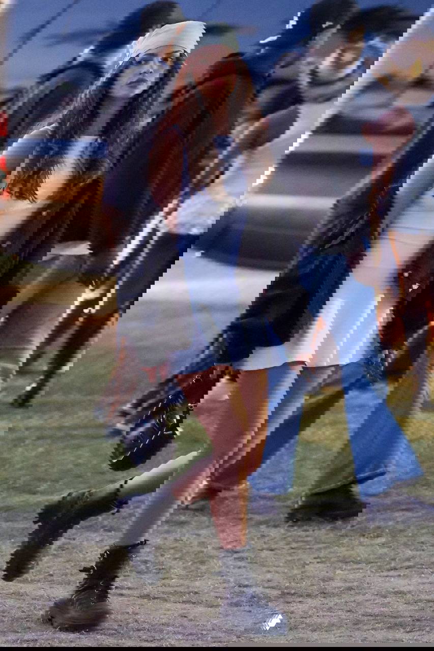 Посетительница фестиваля в белом платье и бандане идёт по поляне среди толпы: непринуждённый образ на фоне людей и машин.