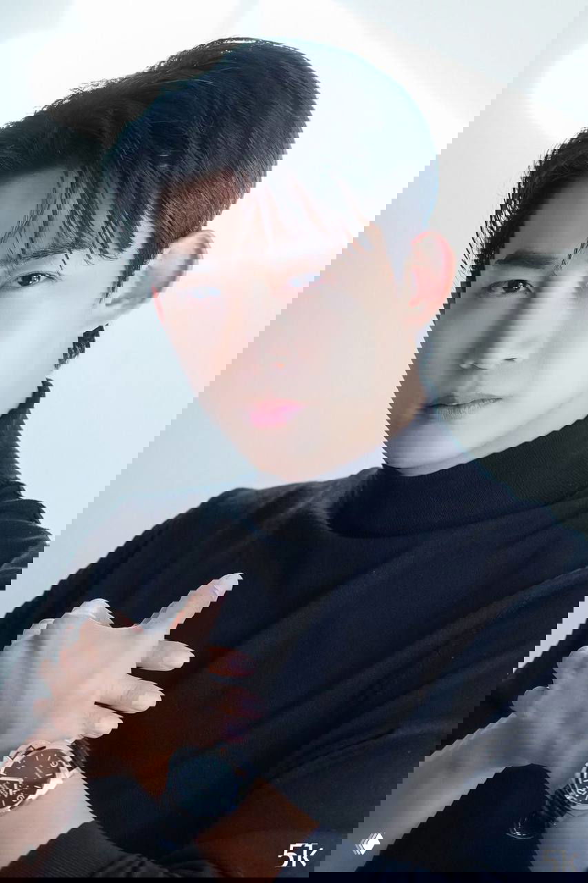 Портретное фото Ок Тэкёна в чёрном гольфе, артист смотрит в камеру; свет подчёркивает черты лица и серьёзное выражение.