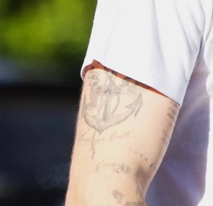 Крупный план предплечья с татуировкой: изображение якоря, надписи и блеклые линии рисунка на светлой коже, отчетливо видны контуры и детали.