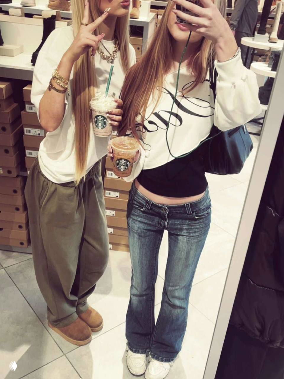 Сэлфи в примерочной: две девушки в низкой талии джинсах и широких штанах, держат напитки Starbucks; типичные детали стиля 2010-х годов.