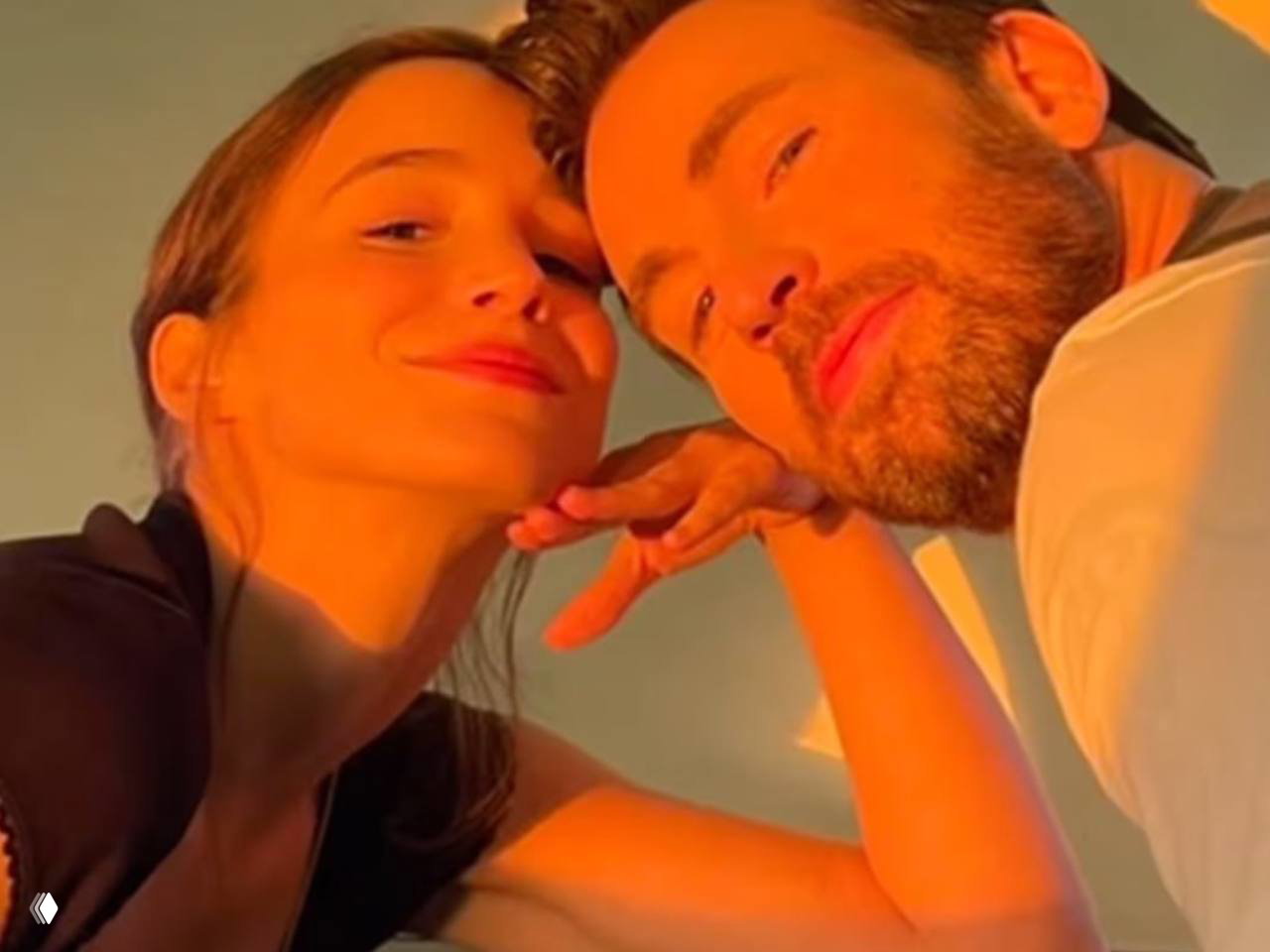 Кадр Криса Эванса и Альбы Баптиста крупным планом на тёплом закатном свете; пара улыбается и позирует вместе, иллюстрация новости о рождении дочери.