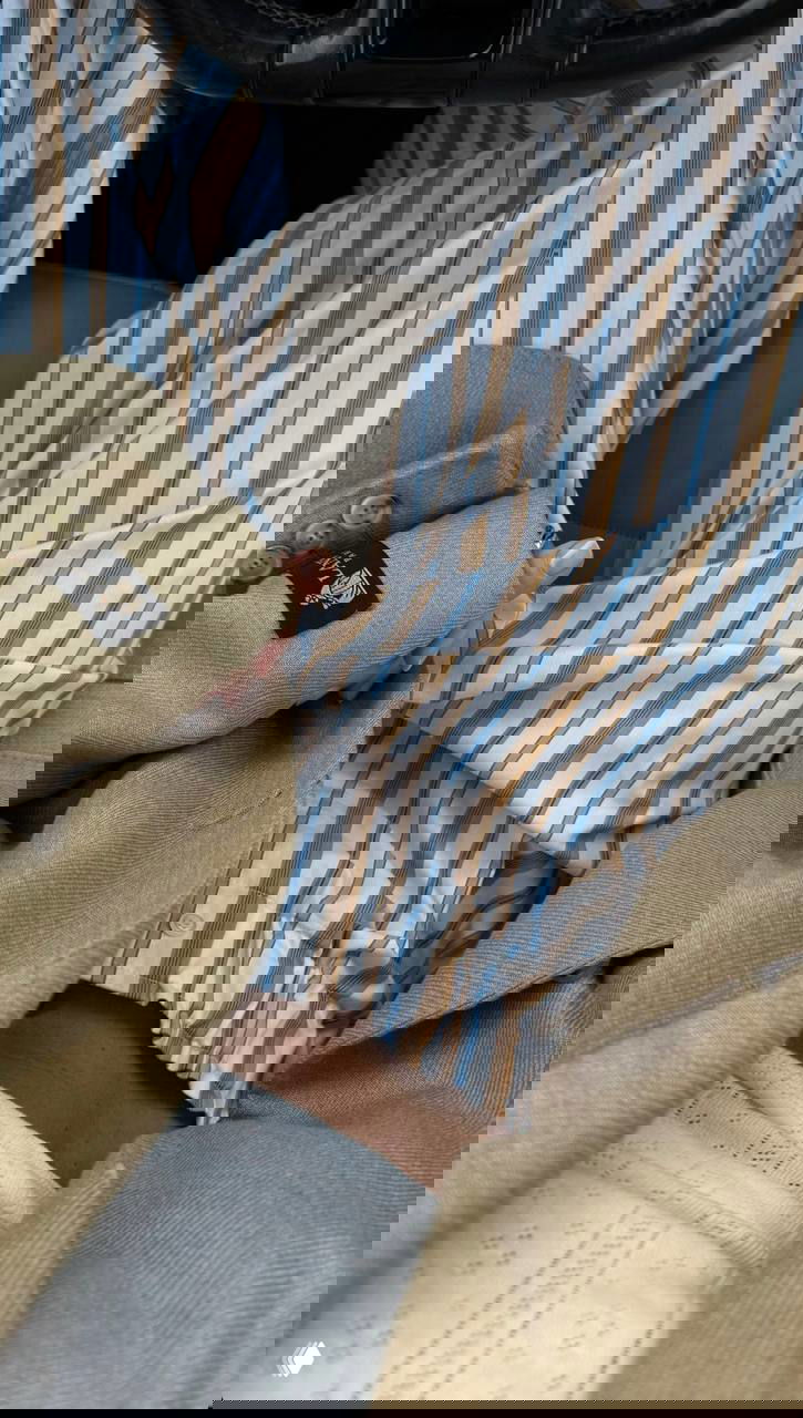 Крупный план: полосатые брюки в бежево-голубую полоску в сочетании с бежевым пиджаком — деталь повседневного образа.