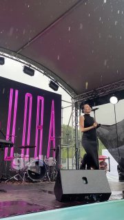 Маша Кольцова выступает на крытой сцене сап‑фестиваля «ЭТО САП, Москва» в дождливую погоду; видны барабаны, микрофон и элементы сцены.