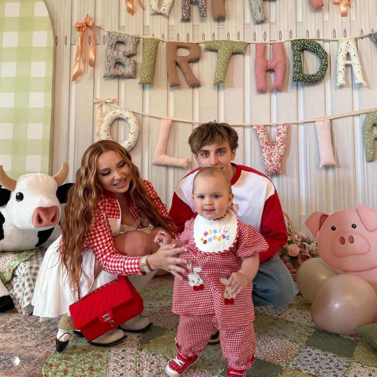 Семейный кадр: пара и маленькая девочка в праздничной декорации с буквами 'BIRTHDAY', мягкими игрушками и воздушными шарами, атмосфера праздника.