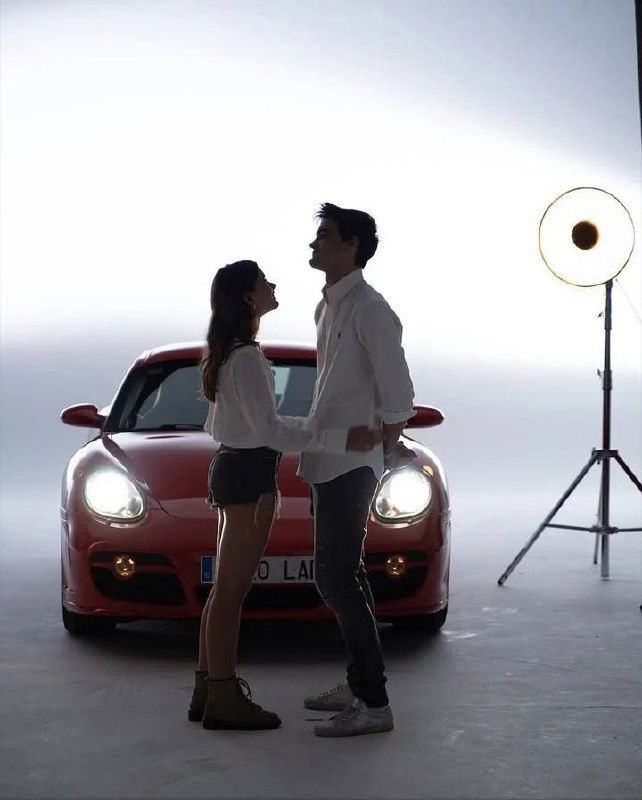 Силуэтная сцена: пара стоит перед красным автомобилем в студии с ярким задним светом и софитом, создавая романтичный силуэтный образ.