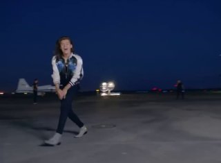Кадр из клипа One Direction: участник идёт по пустой полосе ночью, вдалеке видны огни и фары самолётов, характерная сценография клипа.