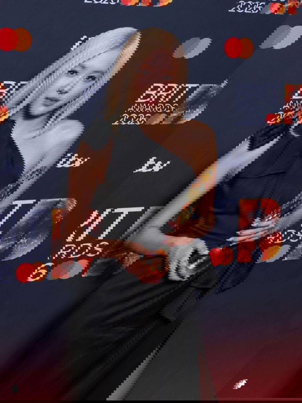 Розэ позирует на фоне пресс-вола BRIT Awards 2026 с наградой в руках, виден бренд BRIT AWARDS и логотипы спонсоров на заднике.