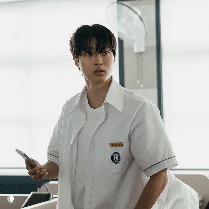 Актёр в школьной форме держит телефон, напряжённый взгляд в интерьерном кадре — сцена из дорамы, ожидаемой в апреле 2026 года.