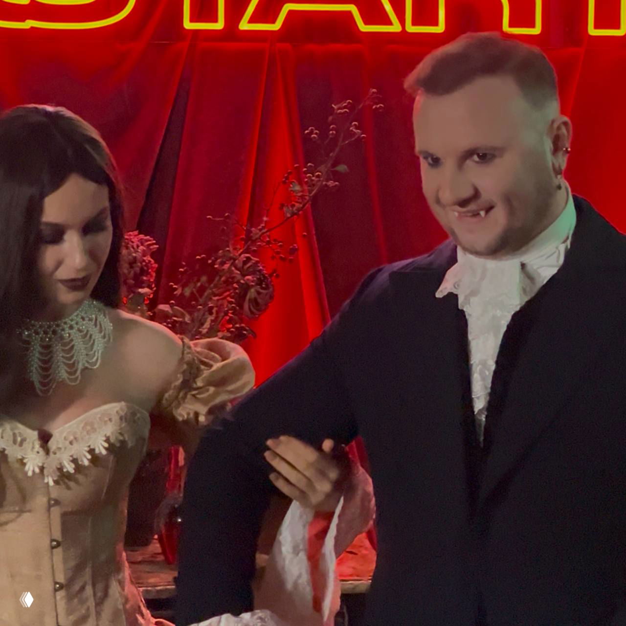 Двое актёров в костюмах — женщина в корсете и мужчина в классическом наряде с искусственными клыками — момент съемки на презентации сериала.