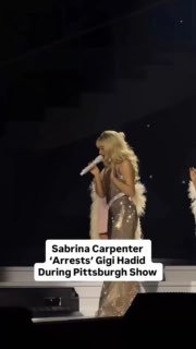 Артистка в блестящем костюме поёт в микрофон на сцене во время шоу; тёмный зал и сценическое освещение, кадр сделан из зрительного ракурса.