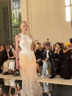 Кадр с кутюрного показа в Париже: модель в белом корсете Schiaparelli и персиковой бахроме идёт по подиуму на показе.