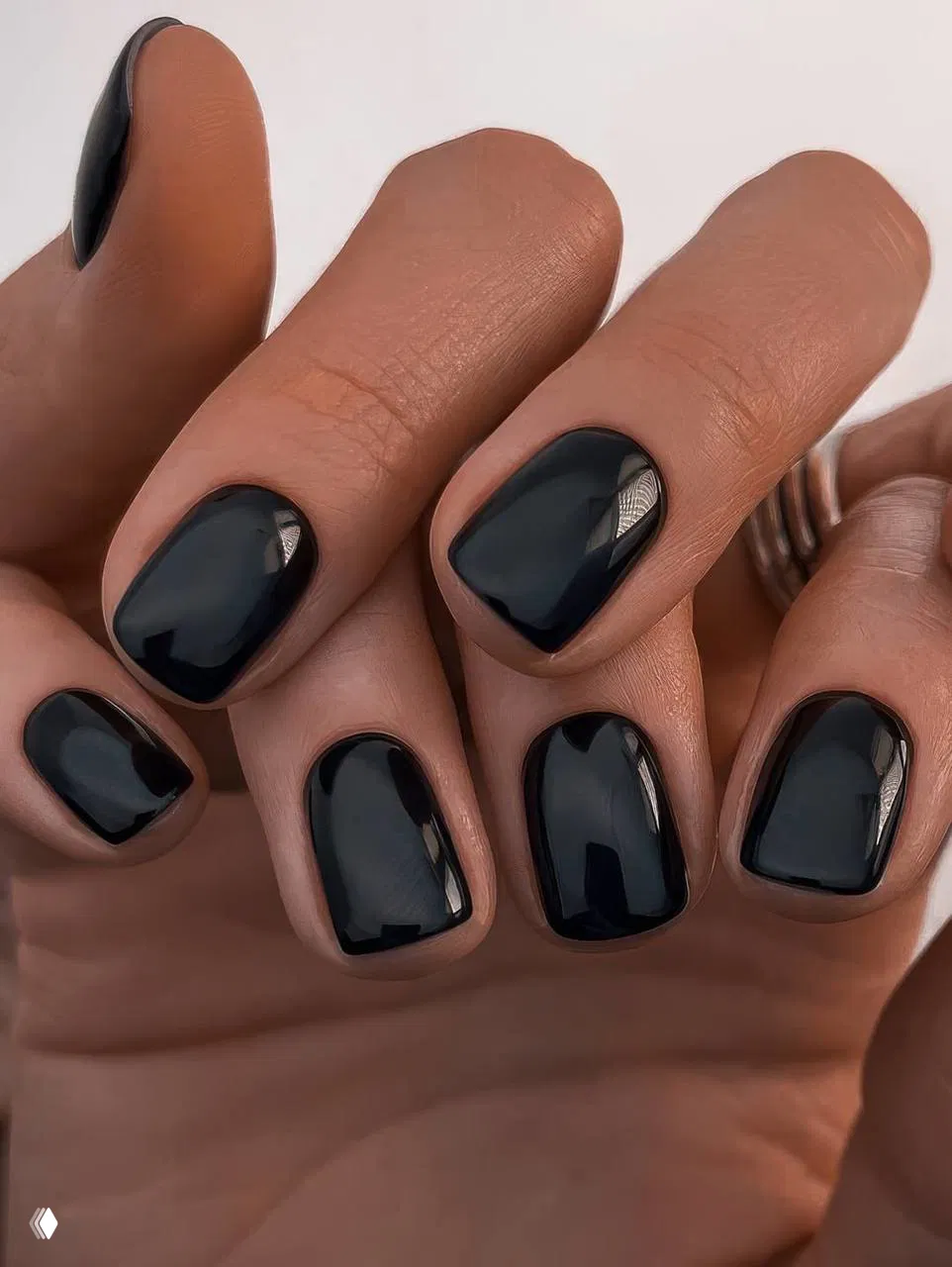Крупный план коротких квадратных ногтей с глянцевым чёрным покрытием на фоне кожи — минималистичный тёмный маникюр.