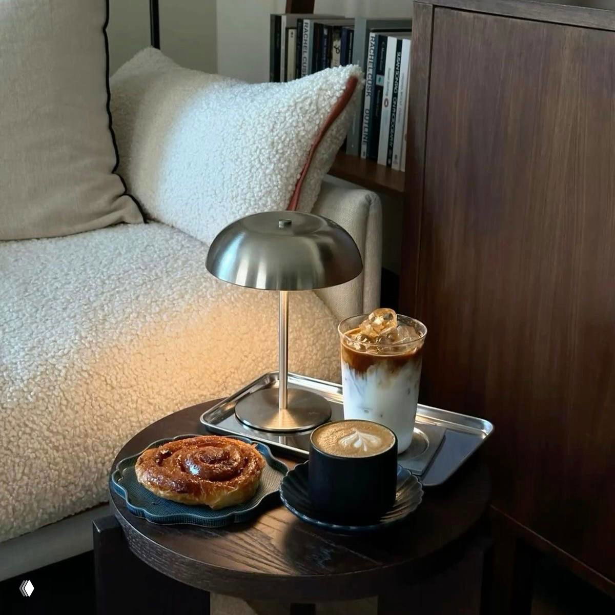 Низкий столик с капучино и айс‑латте рядом со свежей булочкой на фоне тёплого пледа и книжной полки — уютное кафе дома