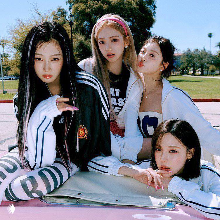 Промо-фото K-pop женской группы: четыре участницы в спортивных и повседневных образах на открытом воздухе, яркий дневной кадр в летней палитре.