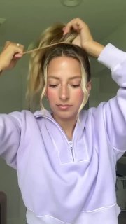 Фронтальный кадр девушки, разделяющей пряди у лица и фиксирующей их заколкой или лентой, отображение лёгкой, непринуждённой школьной укладки.