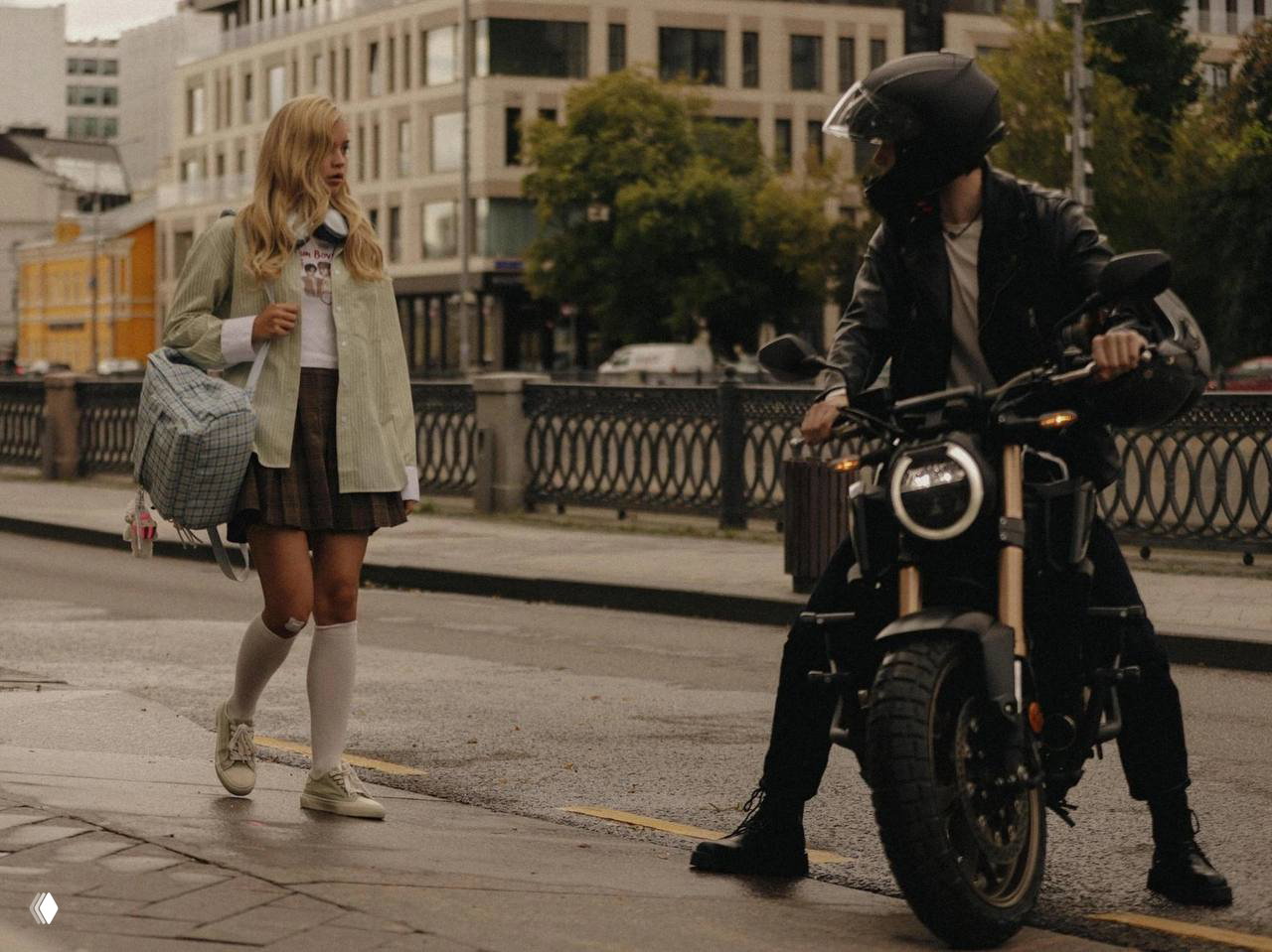 Кадр из фильма: девушка в школьной форме идёт по городской улице и встречает мотоциклиста в защитном шлеме на перекрёстке.