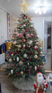 Высокая украшенная рождественская ёлка в гостиной с игрушками, звезда сверху и праздничное убранство комнаты в новогоднем стиле