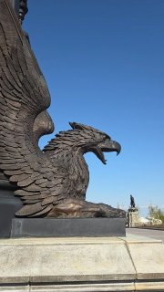Крупный силуэт орла-скульптуры на фоне чистого голубого неба — декоративная бронзовая фигура на ограждении возле замка.
