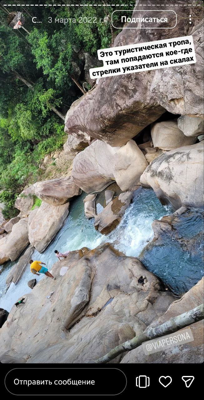 Тропа между крупными скалами над рекой, местами видны стрелки и указатели на камнях, люди перебираются по камням в сторону верхних каскадов водопадов.