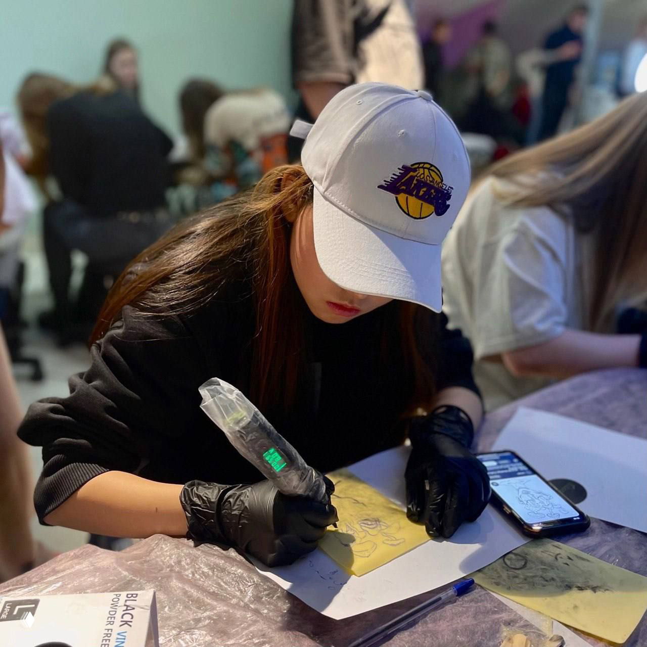 Молодая участница в кепке отрабатывает технику на тренировочной поверхности: сосредоточенность, перчатки и бумажные эскизы рядом.