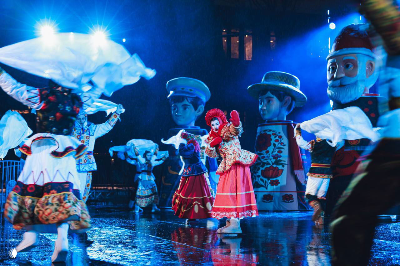 Хоровая и хореографическая сцена с развевающимися платками, подсветкой и большими фигурами месяцев на открытой сцене сада «Эрмитаж».