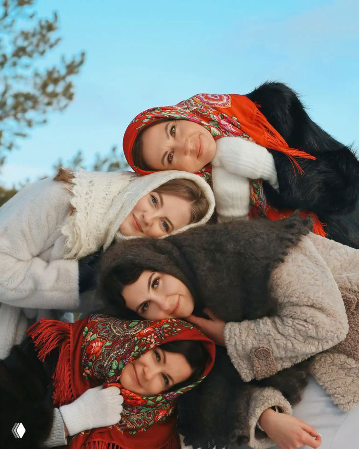 Четыре улыбающиеся женщины в ярких платках и тёплой одежде лежат в снегу, создавая тёплую дружескую композицию и ощущение уюта в поездке.