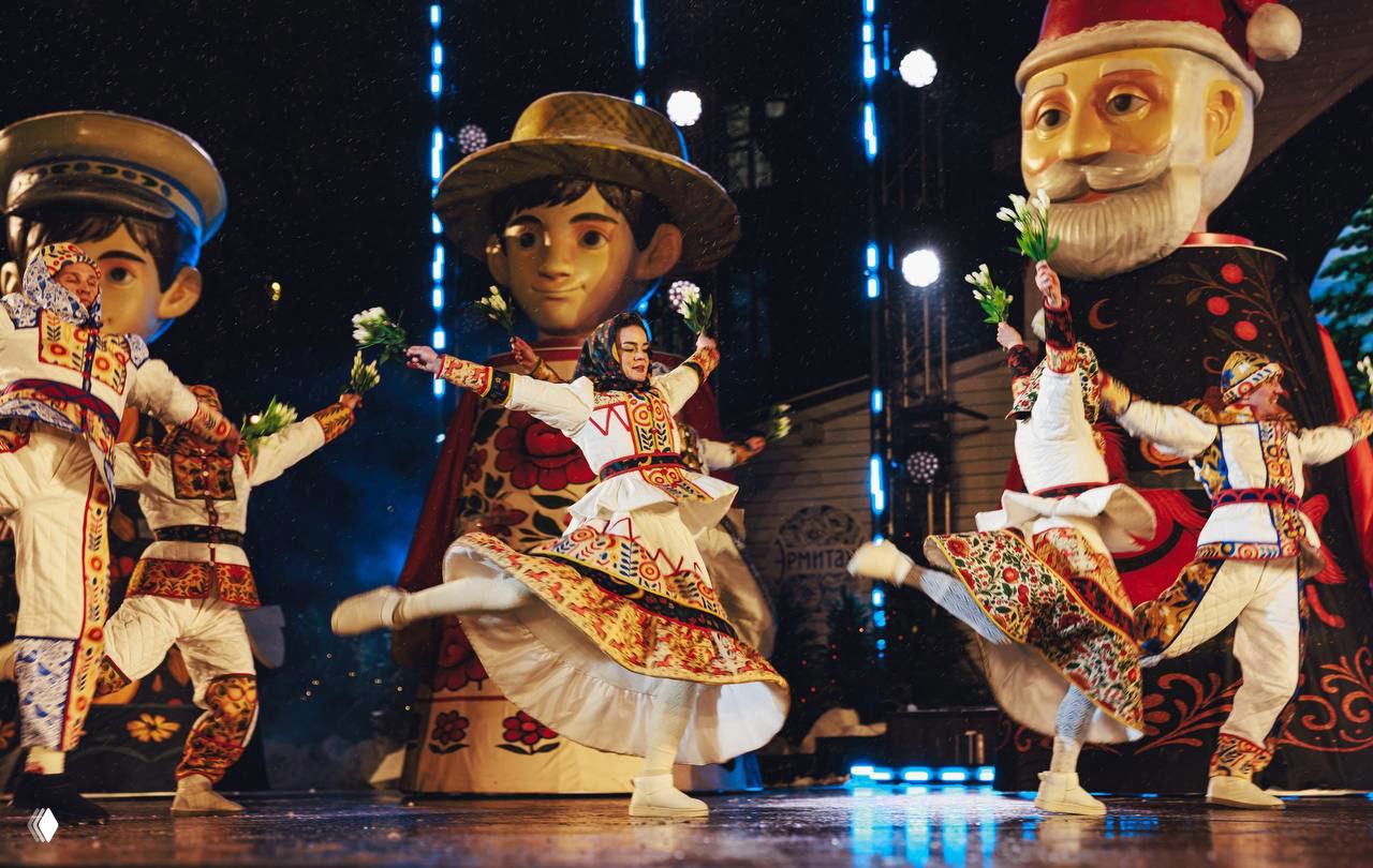 Танцы в традиционном русском стиле: артисты в расшитых костюмах выполняют прыжки и вращения на мокрой сцене под световыми эффектами.