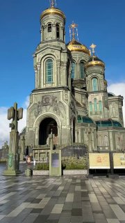 Крупный план архитектуры Храма Вооружённых сил: фасад и купол на фоне чистого синего неба, видна зелёная и каменная отделка здания и элементы декора.