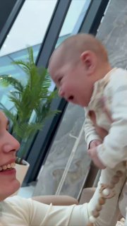 Младенец на руках у взрослого в светлом помещении, вертикальный кадр показывает радостную атмосферу и семейные моменты во время отдыха в отеле.