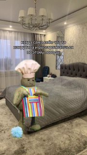 Мягкая игрушка в виде кота стоит на ковре в спальне рядом с кроватью, держит пакет; картинка иллюстрирует шутливую тему фрустрации.