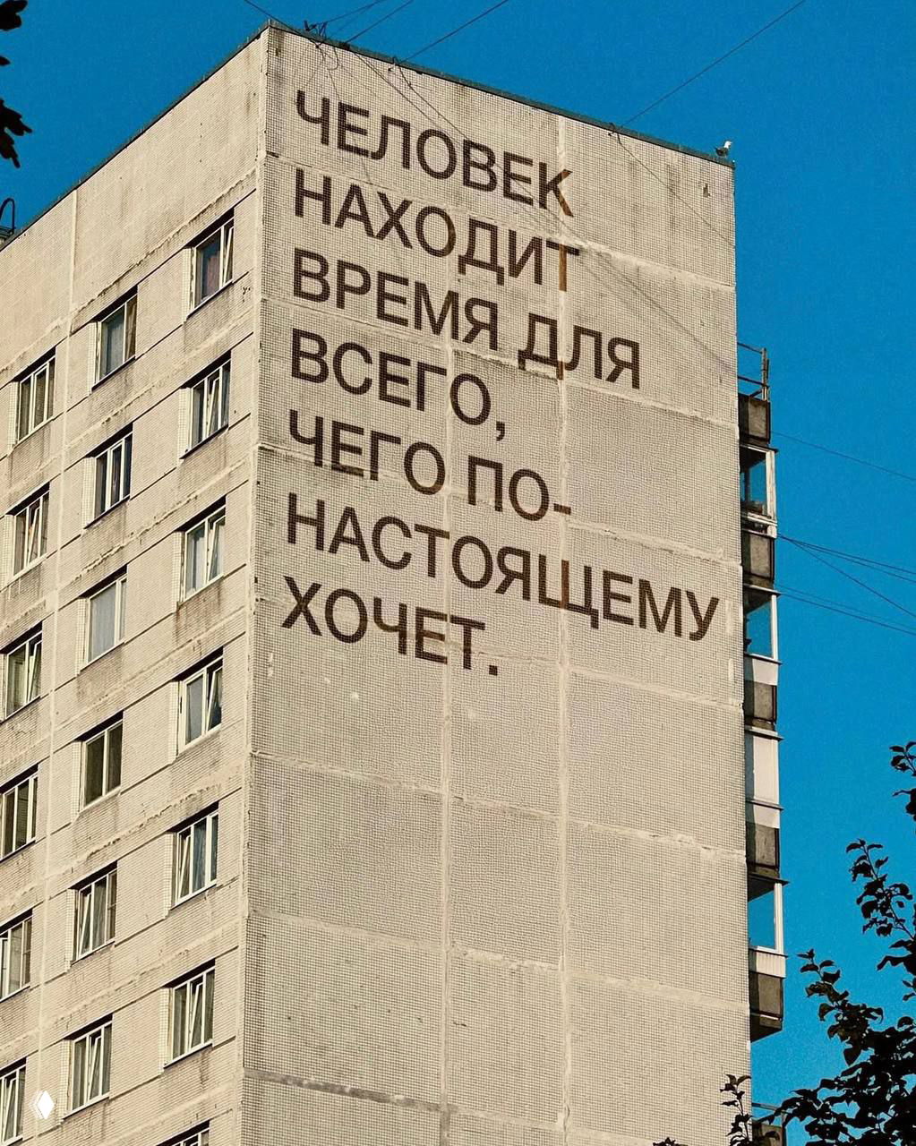 Фотография фасада дома с большой печатной надписью: человек находит время для того, чего по-настоящему хочет — мотивационный слоган на фоне города.