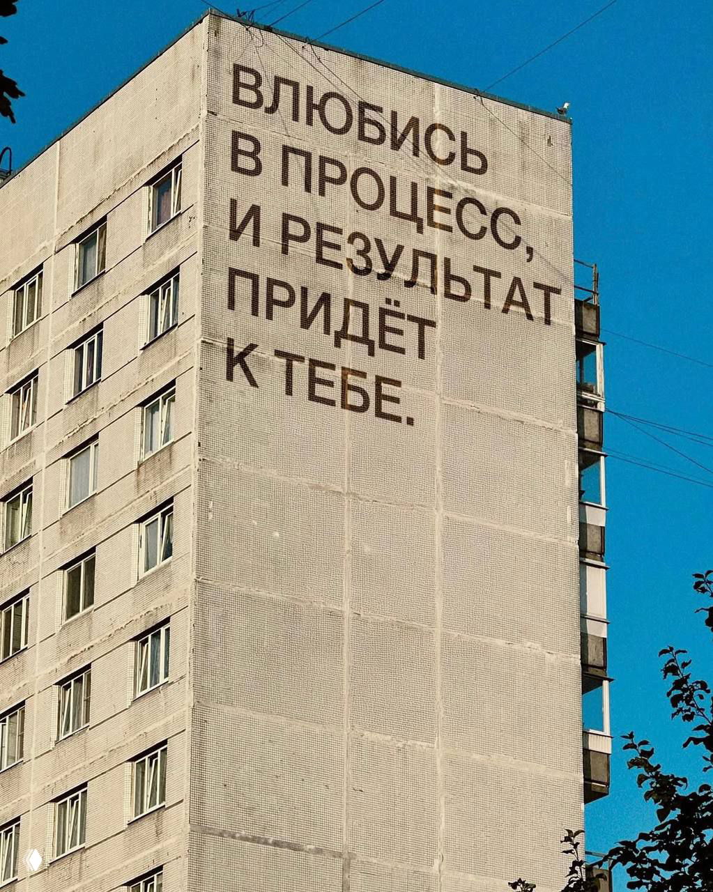 Фасад с мотивационной фразой: «Влюбись в процесс, и результат придёт к тебе», крупная типографика на стене дома, городская сцена.