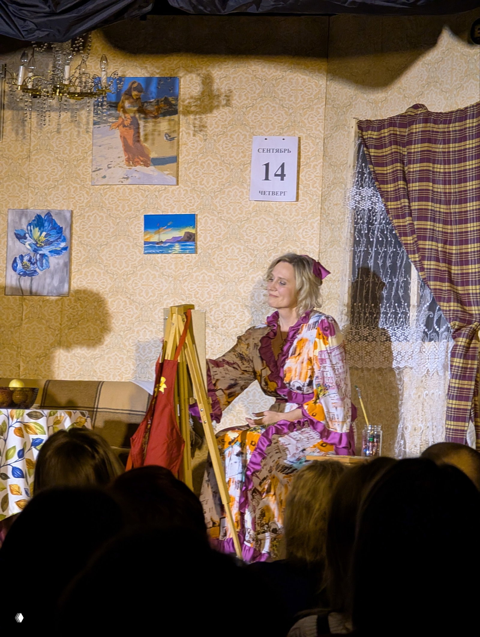 Актриса сидит у мольберта на фоне занавески и календаря с датой 14 сентября — интерьер гостиной в камерной постановке.