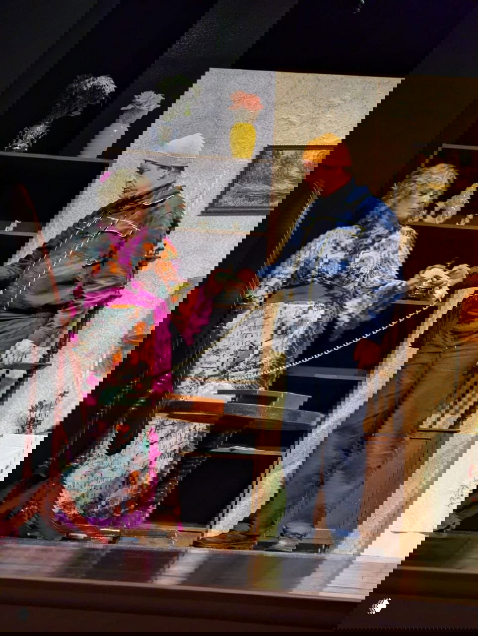 Сцена спектакля в интерьере: женщина в ярком халате с фиолетовым поясом берёт телефонную трубку, перед ней мужчина в рабочей одежде на сцене.