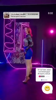 Женщина в студии на фоне неоновых вывесок и розового освещения, кадр из видео с танцем и наложенным текстом.