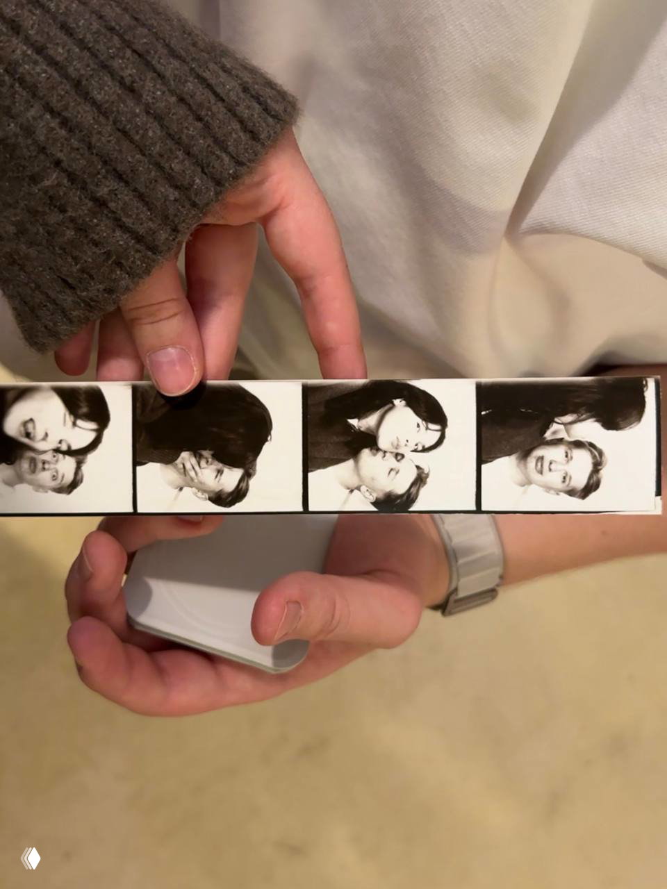 Руки держат фотополоску с чёрно‑белыми кадрами пары и устройство в руке, сувенирная фотополоска как романтичный подарок.