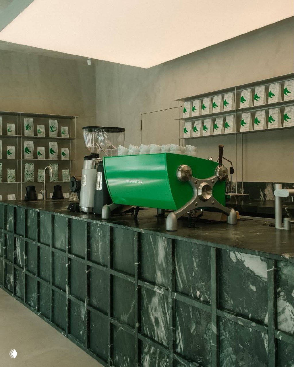 Крупный план зелёной профессиональной кофемашины с логотипом Wildkaffee на мраморной стойке в минималистичном кафе-ринге Вены.