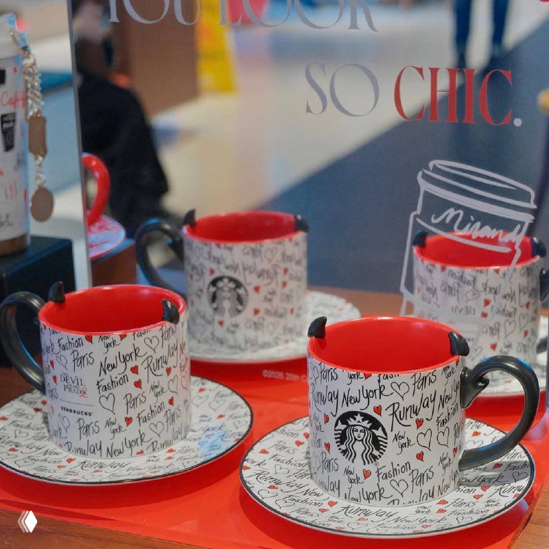 Кофейные чашки и блюдца Starbucks с графичным принтом, красной внутренней поверхностью и декоративными «рогами» на краю чашки на витрине.