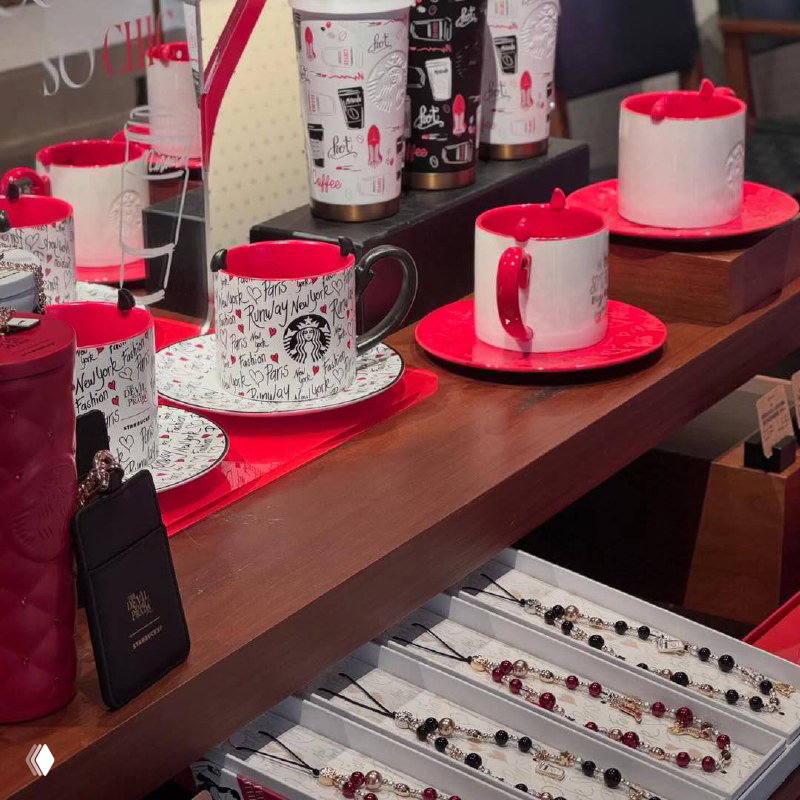 Витрина со стаканчиками и кружками Starbucks, тёмные ручки и ярко‑красные элементы в оформлении, расстановка на деревянном столе.
