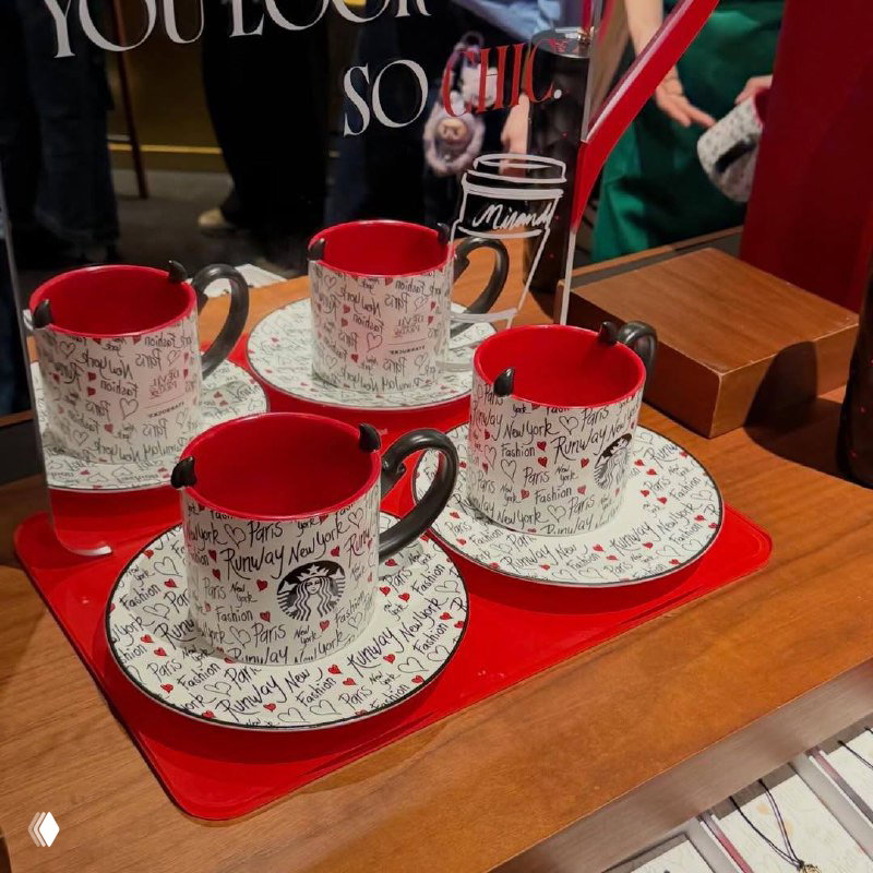 Крупный план белой чашки Starbucks с тиснением логотипа и ярко‑краслой внутренней поверхностью, на блюдце видны тиснённые надписи.