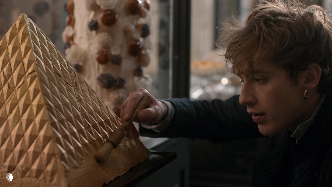 Крупный план героя в кухонной обстановке: молодой повар в процессе отделки сложного кондитерского изделия в исторической пекарне.