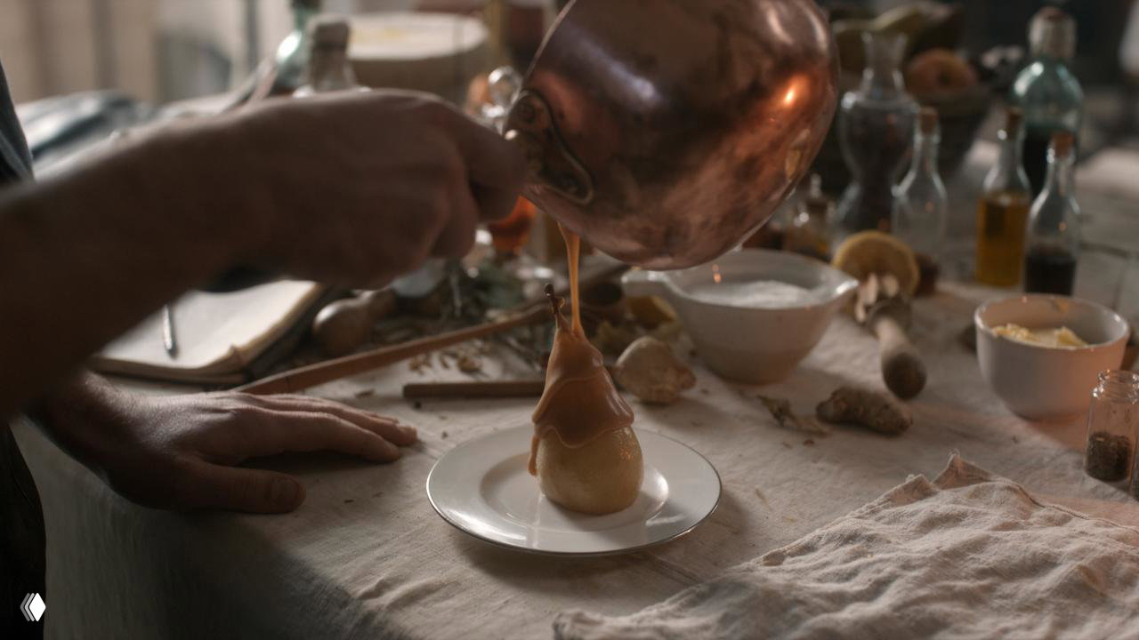 Крупный кадр: сосок с соусом, которого льют на десерт — акцент на текстурах и ручной работе, рабочий стол с кухонной утварью.