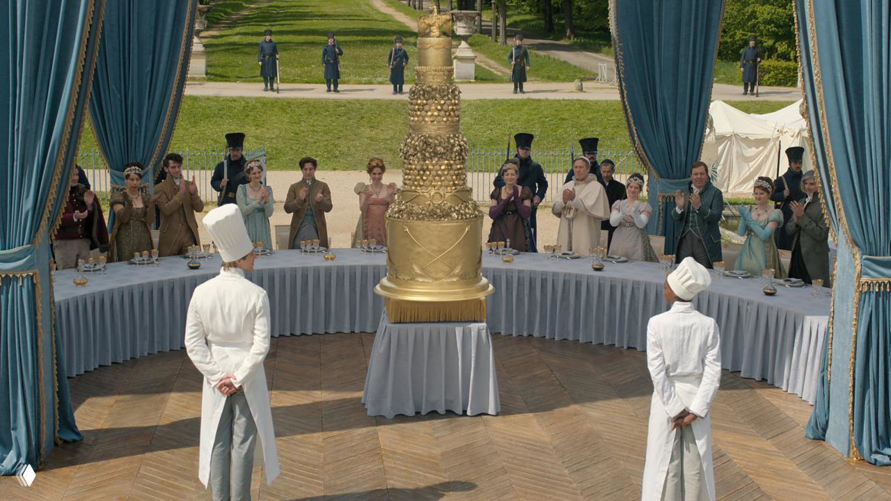 Парадная сцена на открытом воздухе с огромной многоярусной кондитерской конструкцией в центре и застольем вокруг — масштабный фуршет.