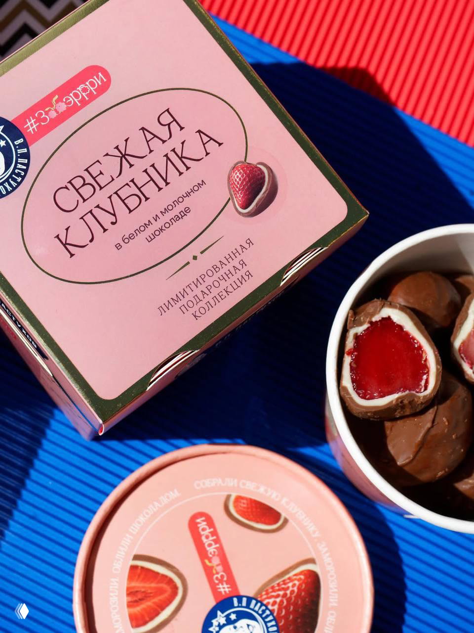Коробка «Свежая клубника» в розовой гамме и открытая чашка с конфетами, видна текстура упаковки и разрезы начинок — демонстрация оформления и стайлинга.