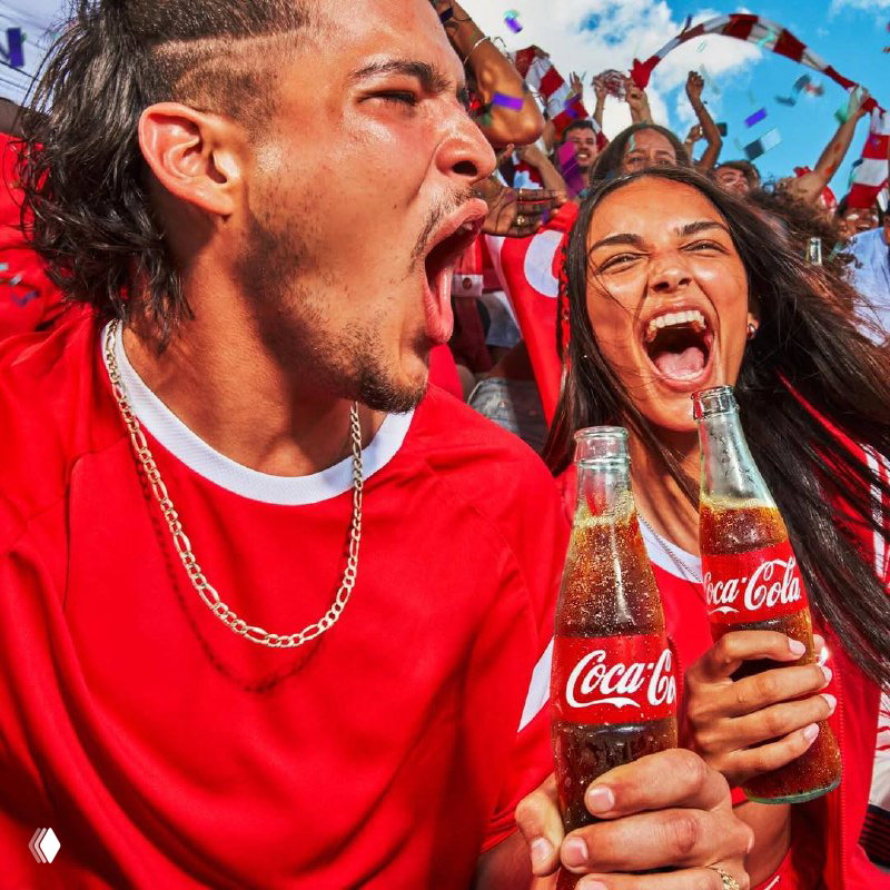 Двое молодых людей кричат и улыбаются, держа бутылки Coca‑Cola — рекламный портрет живой фанатской энергии и бренда на стадионе.