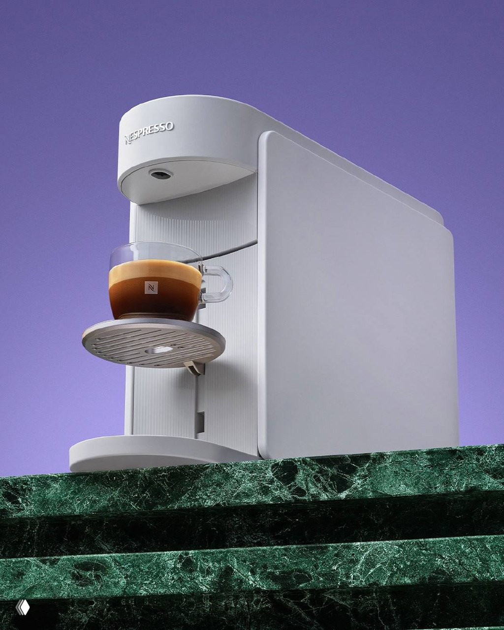 Крупный план белой кофемашины Nespresso на фиолетовой подставке, чашка с тёмной пеной аккуратно расположена на подставке — лаконичная предметная съёмка.