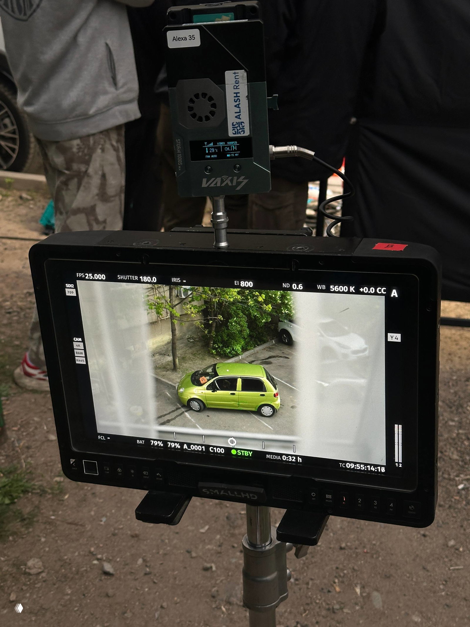 Монитор оператора с кадром зелёной машины на экране и подключённым киносъёмочным оборудованием — бекстейдж уличной съёмки.