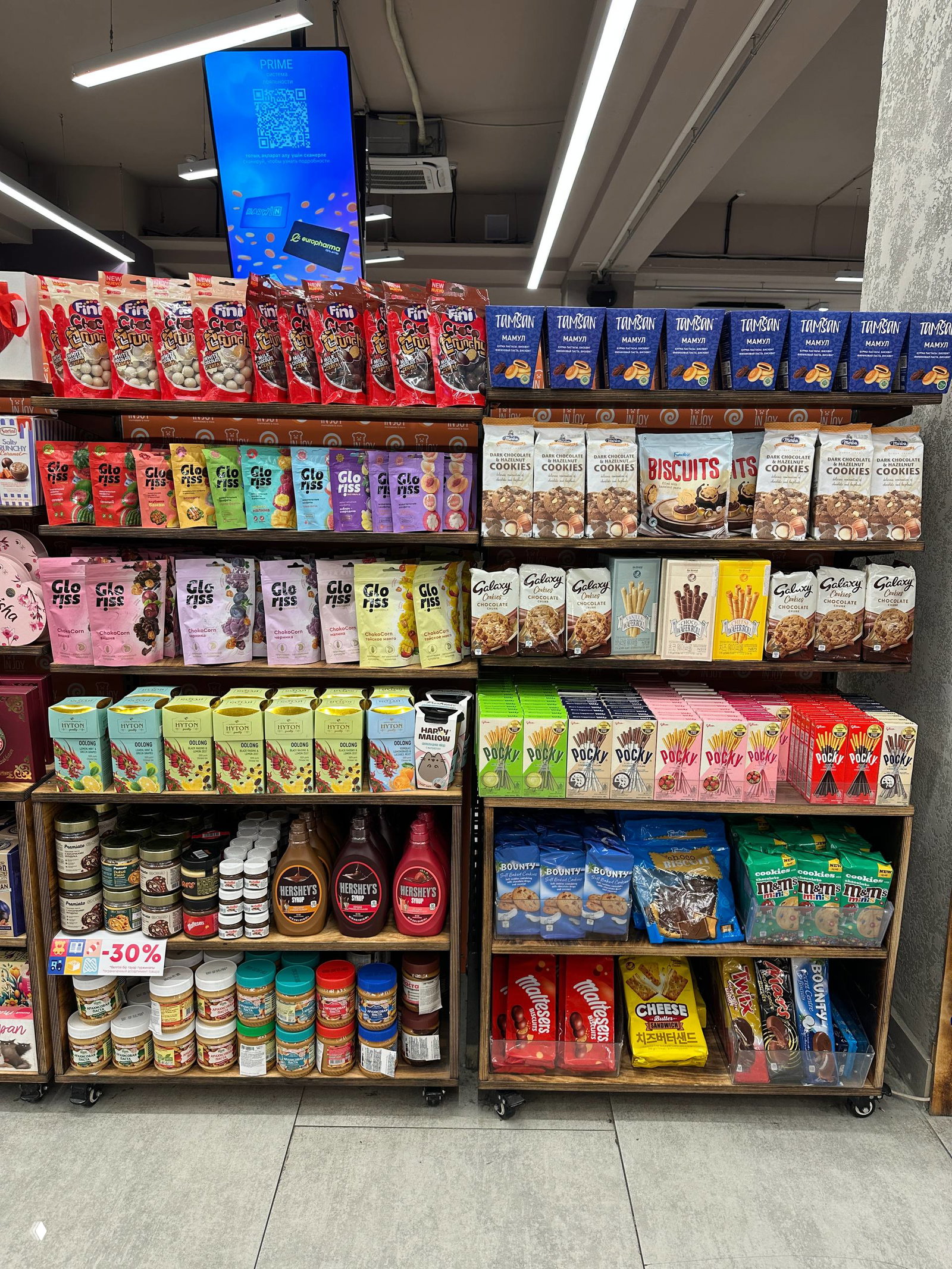 Полки с импортными сладостями и закусками: разноцветные пакеты, коробки и баночки разных брендов, аккуратно выставленные на деревянных стеллажах.